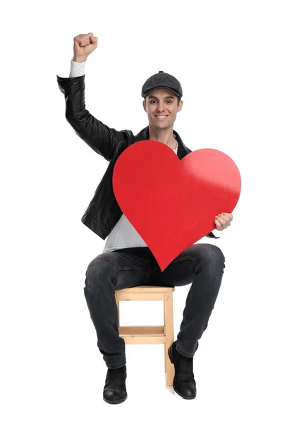 Sentado hombre casual sosteniendo un gran corazón rojo levantando puño — Foto de Stock