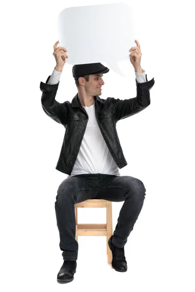 Sedící příležitostný muž držící nad hlavou řeč a dívá se SID — Stock fotografie