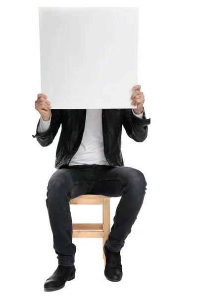 Сидячий випадковий чоловік прикриває обличчя білбордом — стокове фото