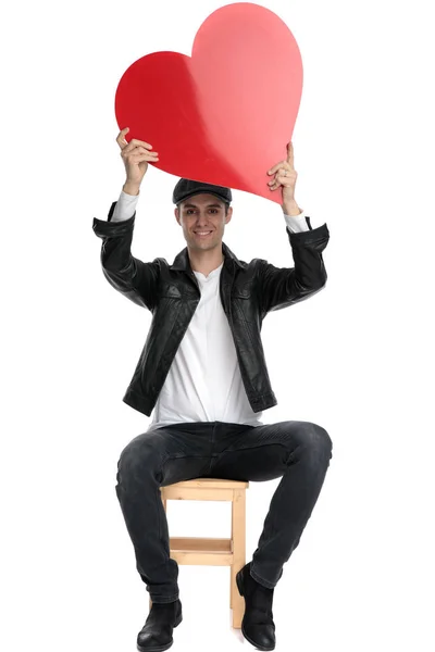 Seated casual man holding a big red heart overhead happy Stock Picture