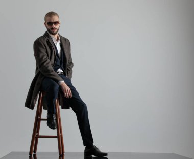 bir eliyle cebinde oturan işadamı kameraya bakıyor