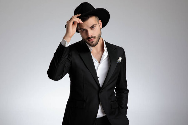 elegant young model holding hat and saluting on grey background