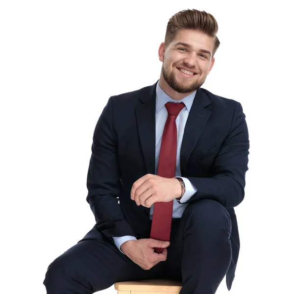 Збуджений молодий бізнесмен тримає краватку і сидить в студії — стокове фото