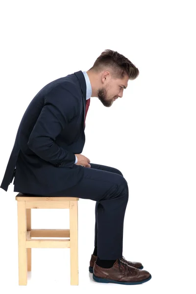 Вид сбоку молодого бизнесмена, сидящего на деревянном стуле — стоковое фото