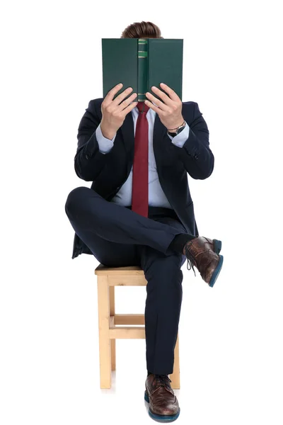 Young businessman hiding behind book in studio — Stock Photo, Image