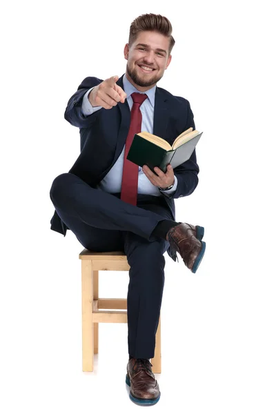 Joven confiado señalando con el dedo y sosteniendo libro — Foto de Stock