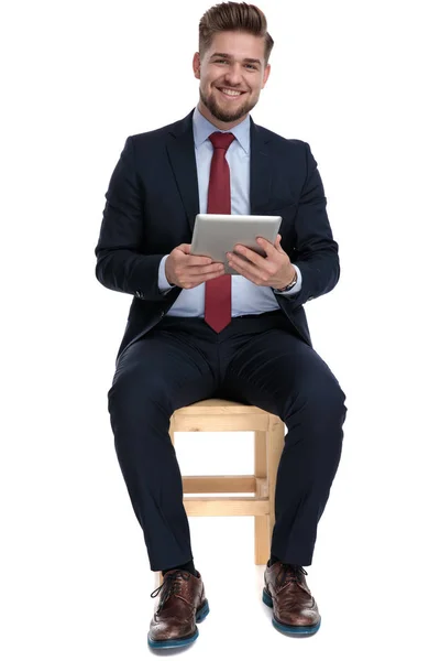 Feliz joven empresario sosteniendo la pestaña y sentado en el estudio — Foto de Stock