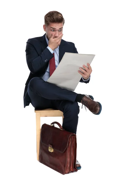 Shocked young businessman reading newspaper in studio — Stock Photo, Image