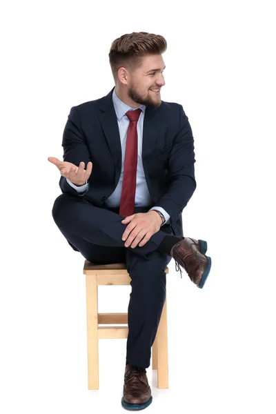Happy young businessman sitting on wooden chair in studio — Stock Photo, Image