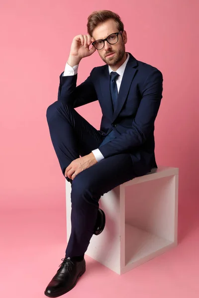 Businessman sitting with one leg resting on chair fixing glasses — Stock Photo, Image