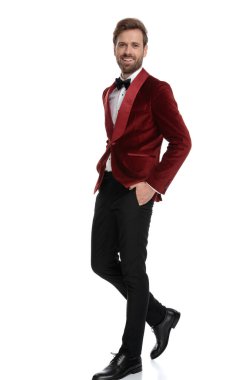 Gülümseyen damat kırmızı kadife smokin giyiyor ve yürüyor.