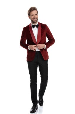 Gülümseyen damat beyaz arka planda kırmızı kadife ceket düzenliyor.