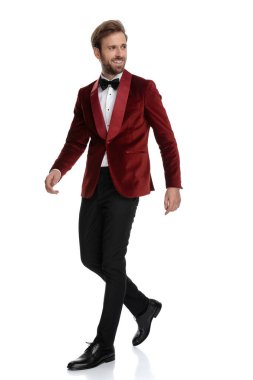 Gülümseyen damat kırmızı kadife smokin giyiyor ve yürüyor.