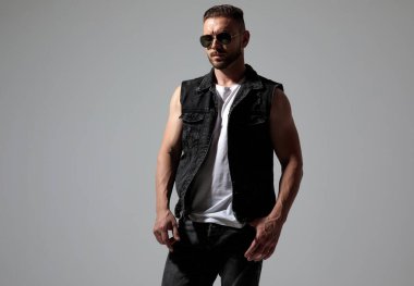 Güneş gözlüğü ve kot yelek giyen ciddi görünümlü bir adam.