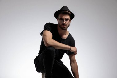 Sıradan bir adam bir eli dizinde çömelmiş şekilde ayakta duruyor.