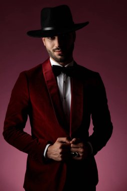 Mutlu moda adamı pembe arka planda kırmızı kadife ceket çekiyor.