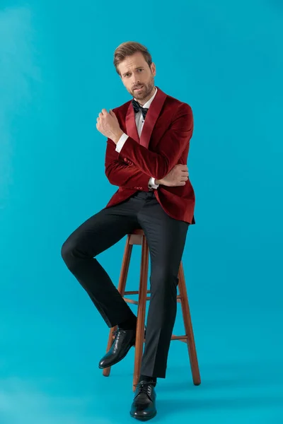 Elegancki mężczyzna moda siedzi i nosi czerwony aksamit smokingu — Zdjęcie stockowe