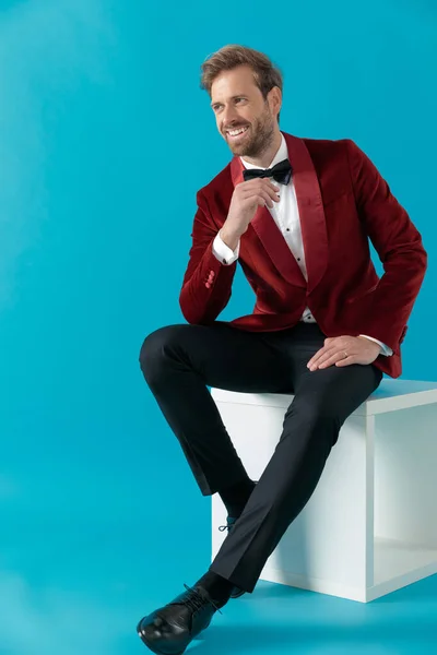 Modelo de moda sorridente sentado e vestindo smoking de veludo vermelho — Fotografia de Stock