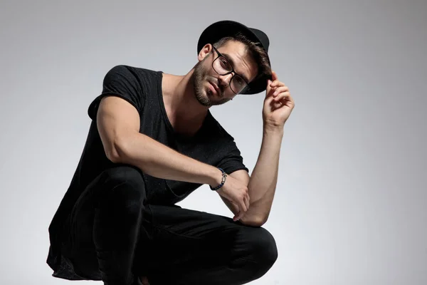 Casual man standing crouched and fixing his hat — Stock Photo, Image