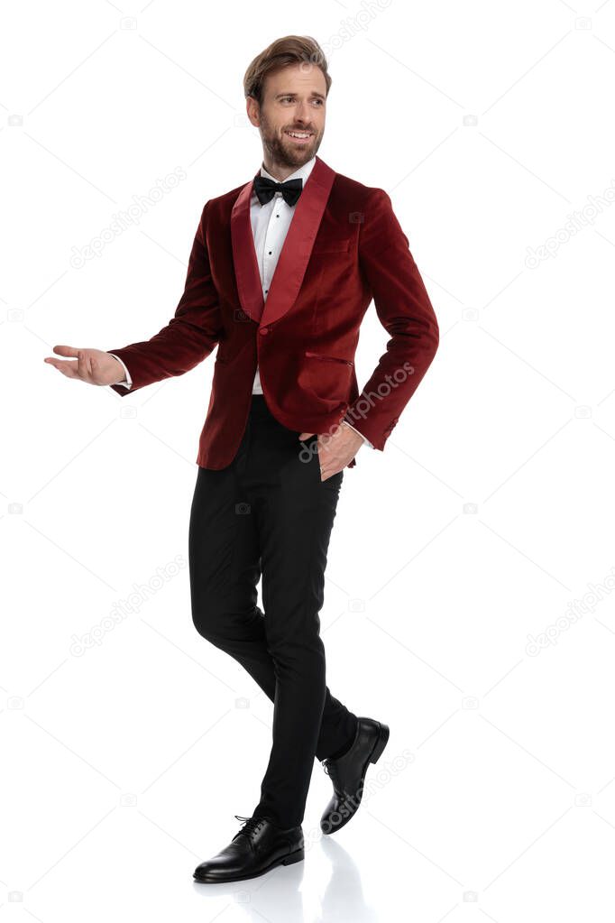 happy young fashion man wearing red velvet tuxedo and presenting