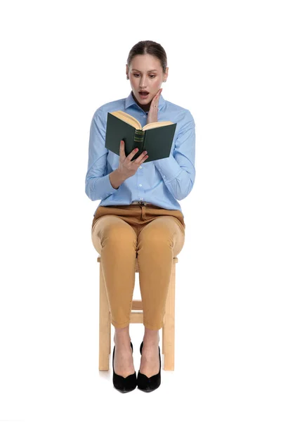 Zaskoczona młoda kobieta czytania książki i trzymając się za rękę do policzka — Zdjęcie stockowe