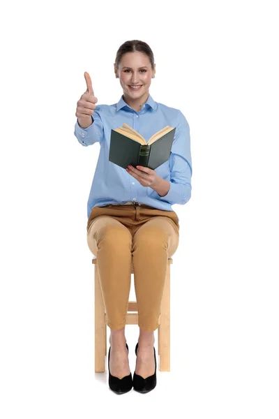 Feliz joven mujer sosteniendo libro y haciendo pulgares hacia arriba signo —  Fotos de Stock