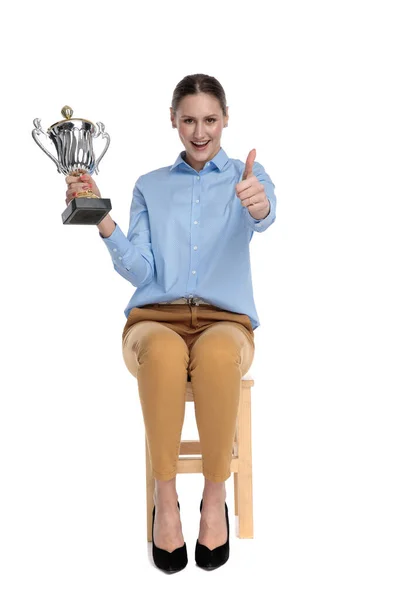 Feliz jovem empresária segurando troféu e fazendo polegares até si — Fotografia de Stock