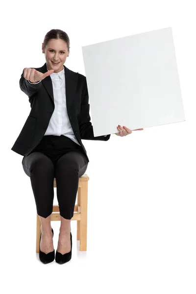 Businesswoman sitting and holding billboard while pointing forwa — Stock Photo, Image