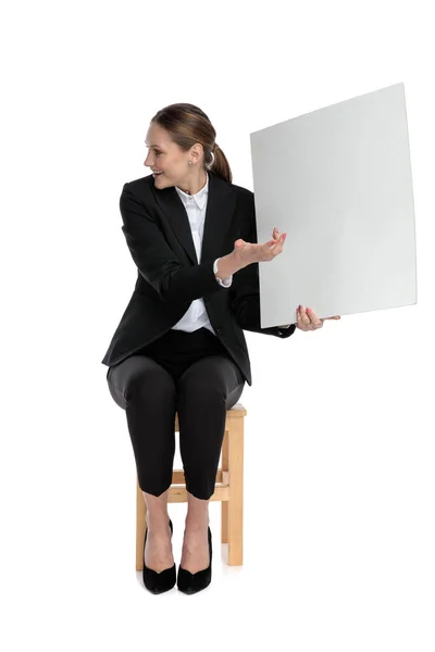 Businesswoman sitting and pointing aside to her billboard — Stock Photo, Image