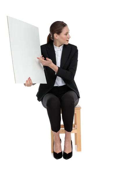 Businesswoman sitting and presenting billboard to a side — Stock Photo, Image