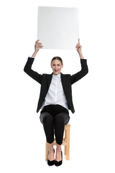 Счастливая деловая женщина сидит и держит рекламный щит над головой — стоковое фото