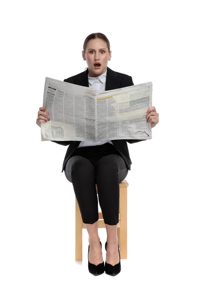 Bizneswoman siedzi i trzyma gazetę w szoku — Zdjęcie stockowe