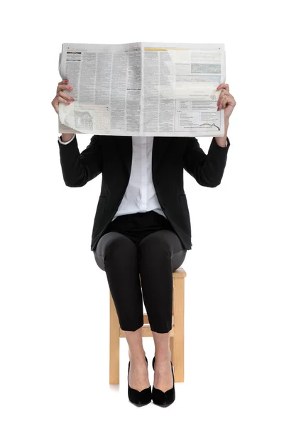 Schüchterne Geschäftsfrau sitzt und versteckt sich hinter Zeitung — Stockfoto