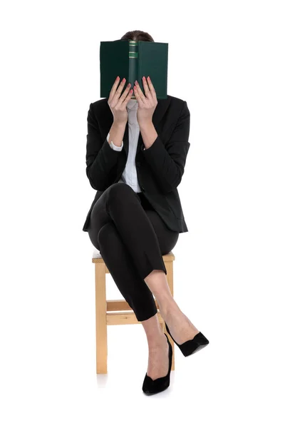 Shy businesswoman sitting and hiding behind a book — Stock Photo, Image