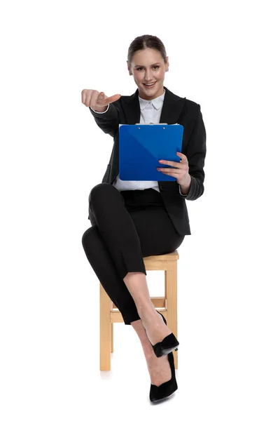 Geschäftsfrau sitzt und hält Klemmbrett, während sie nach vorn zeigt — Stockfoto
