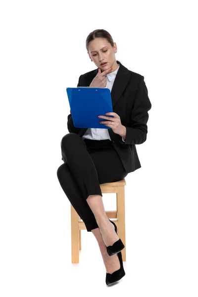 Geschäftsfrau sitzt und liest etwas auf Klemmbrett intrigu — Stockfoto