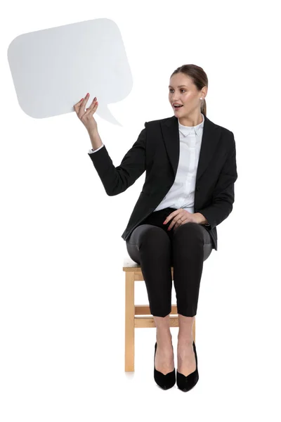 İş kadını oturmuş, elinde konuşma balonu tutuyor ve yardımsever görünüyor. — Stok fotoğraf