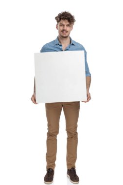 Genç, sıradan bir adam elinde boş bir tahta tutuyordu ve gülümsüyordu. Beyaz arka planda tek başına duruyordu.