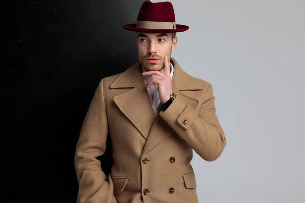 таинственная молодая модель касается щеки и смотрит в сторону, стоя на черном сером фоне
