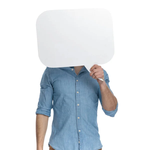 デニムシャツを着た若いカジュアルな男が顔を覆い スピーチバブルで白い背景に孤立して立って 肖像画 — ストック写真
