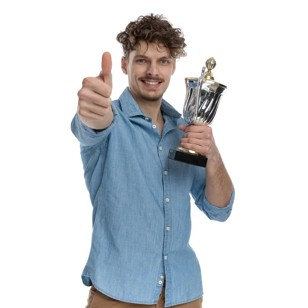 快乐的年轻人拿着奖杯 竖起大拇指 孤零零地站在白色的背景上 — 图库照片