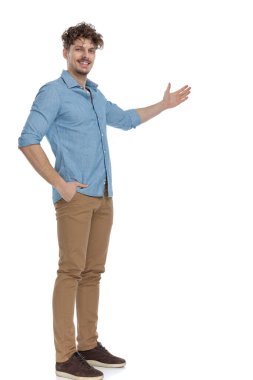 Kot gömlekli mutlu adam yan tarafa davet ediyor ve gülümsüyor, ceplerinde el ele tutuşuyor ve beyaz arka planda izole bir şekilde bekliyor.