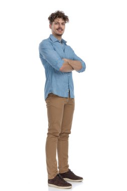 Kot gömlekli genç adam kollarını kavuşturup gülümsüyor beyaz arka planda izole bir şekilde bekliyor.