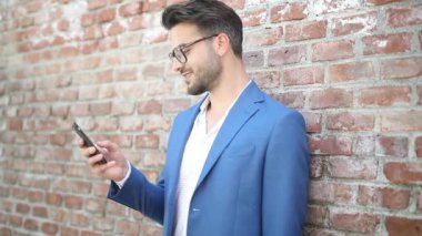 Zeki sıradan iş adamı duvara yaslanıyor, telefonuna bir mesaj yazıyor, gülümsüyor ve yan bakıyor.