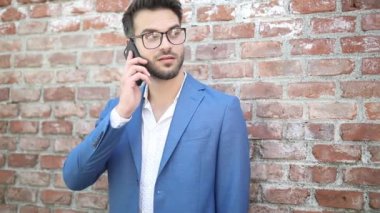 Tuğla duvarda dikilen mutlu iş adamı telefonuna cevap veriyor, gülümsüyor ve etrafa bakıyor.