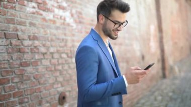 Yakışıklı iş adamı gülümsüyor, telefonuna mesaj atıyor, etrafa bakıyor ve duvara gülüyor.