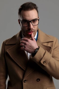 Seksi zeki adam dudaklara dokunuyor ve gri arka planda gözlük takıyor.