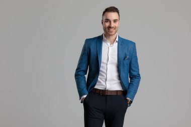 Mutlu genç adam gülümsüyor ve el ele tutuşuyor, gri arka planda duruyor.