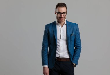 Mutlu genç, zeki, gözlüklü, gülümseyen, el ele tutuşan ve gri arka planda duran adam.