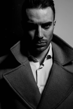 Uzun paltolu dramatik zarif adam siyah gri arka planda gölgede duruyor.